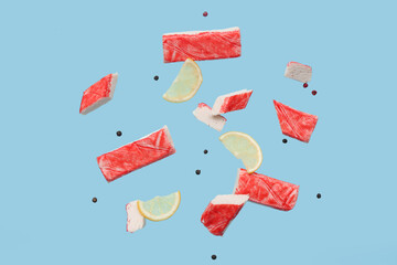 Cut tasty crab sticks with peppercorns and slices of lemon flying on blue background © Pixel-Shot