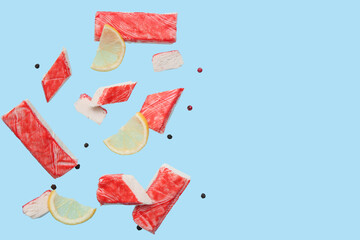 Cut tasty crab sticks with peppercorns and slices of lemon flying on blue background © Pixel-Shot