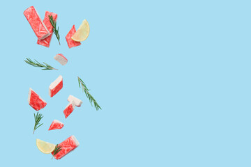 Cut tasty crab sticks with rosemary and slices of lemon flying on blue background © Pixel-Shot