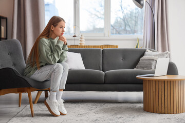 Obraz premium Worried young woman sitting in armchair at home