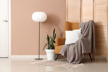 Armchair, lamp and folding screen near brown wall in room