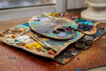 An old palette with oil paints in the artist's studio. Painted background created by a creative person. 