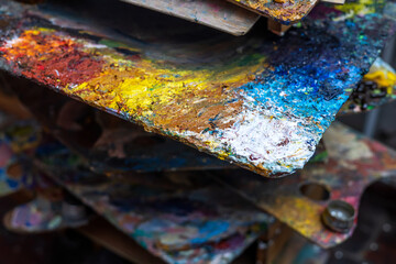 An old palette with oil paints in the artist's studio. Painted background created by a creative person. 