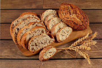 Freshly baked whole grain homemade sourdough bread with crispy crust, sliced and ears of wheat on wooden table, modern baking concept, healthy natural food