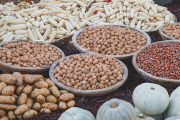 Rustic market display with wooden bowls filled with walnuts and hazelnuts, surrounded by potatoes, pumpkins, and dried corn, representing autumn harvest and organic farming