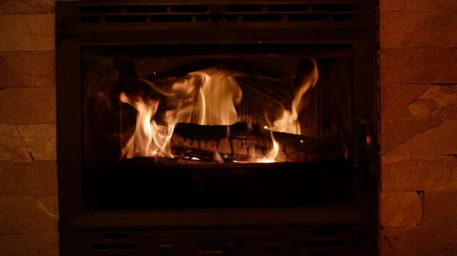 A cozy fireplace crackles with gently flickering flames, reflecting soft light on coffee-beige tiles. The dancing fire adds warmth and subtle glow to the inviting setting.
