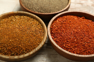 Bowls of aromatic spices on light wooden table, closeup