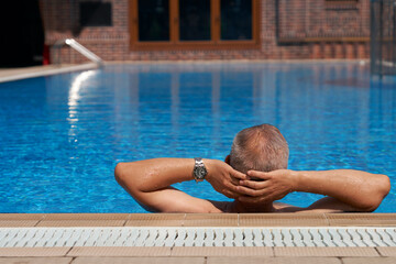 Relaxed adult man in azure water swimming pool. Copy space.