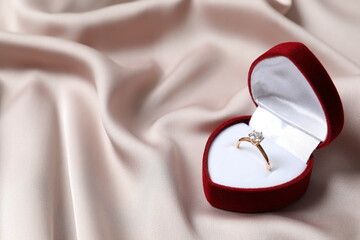 Beautiful shiny gold engagement ring with large diamond gemstone in a rich red velvet box on silk...