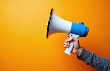Hand holds megaphone for announcement on orange backdrop. Promoting concept involves loud voice and social media alerts. Communication equipment for marketing or public rally events, campaign news.