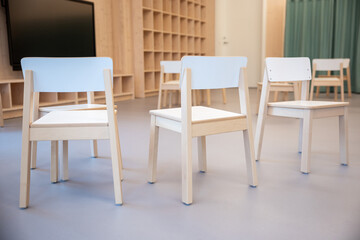 Light wooden chairs with white accents are arranged casually. A wall with cubby shelves and a flat...