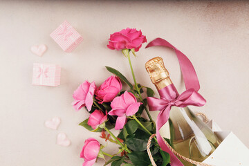 A beautiful still life composition featuring pink roses, a champagne bottle with a pink ribbon, and small wrapped gifts.