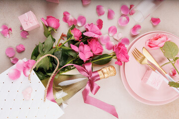 A beautifully arranged romantic dinner table featuring pink roses, a champagne bottle, golden cutlery, and a heart-themed decor.