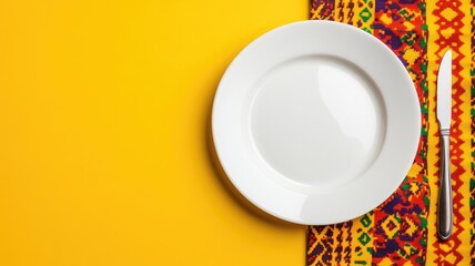 Empty white plate and knife on colorful tablecloth yellow background