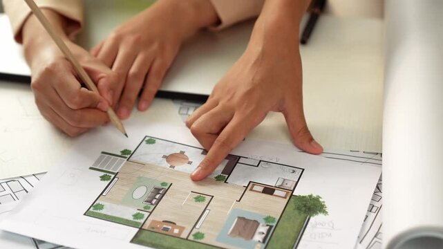 Smart architect and safety engineer discussion about building blueprint on table with architectural document, measurement tools and wooden block scatter around at modern office. Closeup. Delineation.