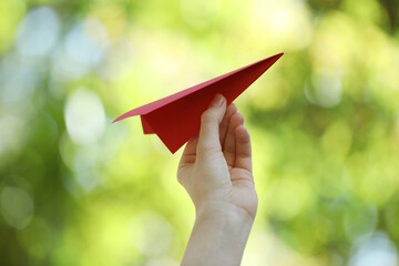 Woman with handmade paper plane on blurred green background, closeup