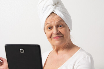 Caucasian senior woman with wrinkles talking with somebody by tablet