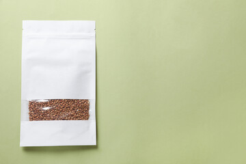 Paper pouch bag with buckwheat on green background, top view. Space for text