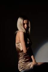 Fototapeta premium beautiful young woman in a golden dress on a dark background.