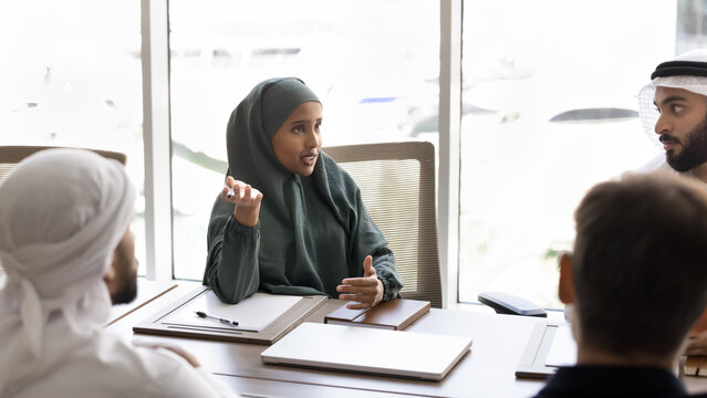 Young Muslim businesswoman dressed in traditional abaya engaged in formal discussion with colleagues or partners, share upcoming tasks and deadlines, consider partnership opportunities, collaboration