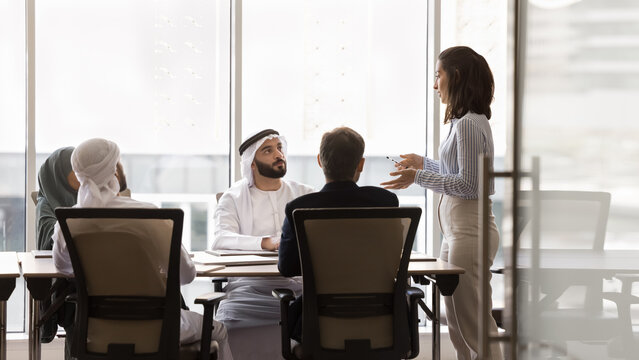 Multinational businesspeople listening speech, presentation of young Brazilian female team leader, presenting review of company performance, gather together for strategy planning, new product launch - Powered by Adobe