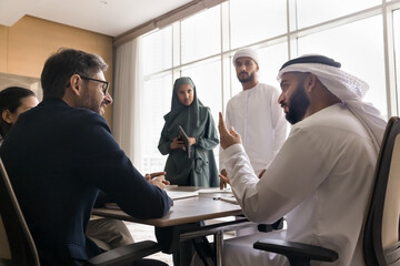 Multicultural businesspeople engaging in group meeting in office. Arabian bankers dressed in traditional dishdasha and abaya hold negotiations with clients, shareholders or investors. Business, deal