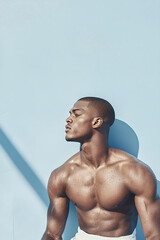 Muscular man basking in sunlight against blue wall  
