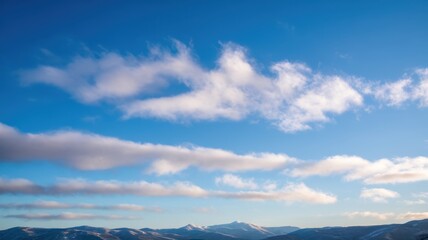Fototapeta premium A breathtaking expanse of vibrant blue sky filled with soft white clouds, overlooking snow-capped mountains in the distance.
