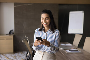 Attractive Brazilian businesswoman using smartphone in boardroom, holding modern gadget, solve...