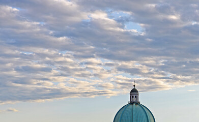Green domed roof with cross of the New Cathedral or Duomo Nuovo with clouded sky on a summer afternoon in Brescia, Italy