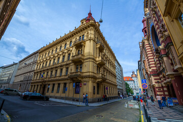 A low-angle shot captures a historic corner building with ornate facade and red roof, under a bright sky, alongside a modern striped building and street signs, in an urban setting