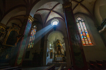 Fototapeta premium Interior view of a church featuring a striking beam of light piercing through the arched architecture, highlighting stained glass windows and ornate details.