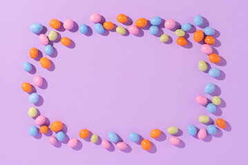 Colorful easter dragee on a violet background. Multicolored candies in the shape of eggs covered with glaze
