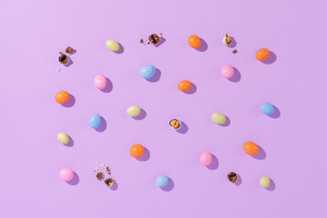 Colorful easter dragee on a violet background. Multicolored candies in the shape of eggs covered with glaze