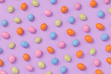 Colorful easter dragee on a violet background. Multicolored candies in the shape of eggs covered with glaze