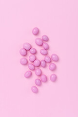 Pink easter dragee on a pink background. Sweet candies in the shape of eggs covered with pink glaze