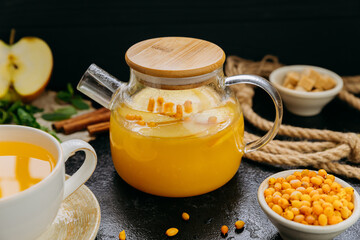 Sea buckthorn tea with apple and mint in glass teapot on rustic background, perfect for wellness