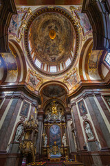 Obraz premium A dramatic interior view of a baroque church featuring a richly decorated dome with a painted ceiling, ornate columns, statues, and a golden chandelier, viewed from a low angle perspective.