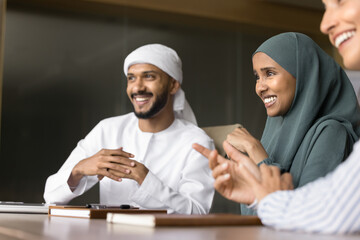 Group of multinational teammates laughing at briefing in office, sit at table enjoy pleasant...