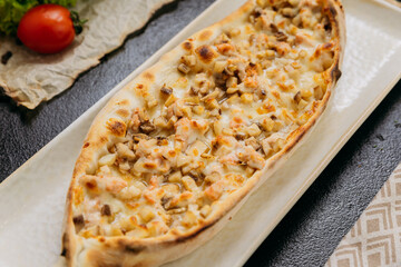Turkish pide with diced chicken, cheese, and vegetables on plate in traditional gourmet presentation