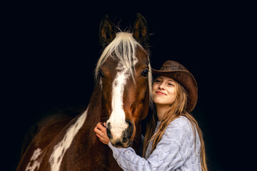 A young teenager girl and her pinto horse cuddling and interacting together in front of black...