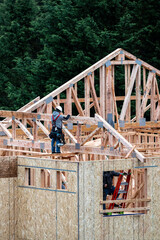 New home under construction in framing phase, workman in hard hat and tool belt with nail gun...