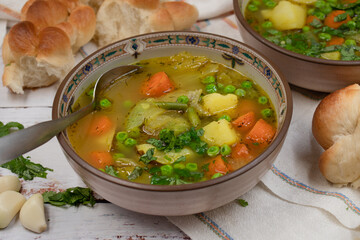 Vegan carrot, potato and peas soup on wooden table, served with braided bread