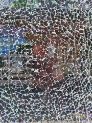 A close-up view of shattered glass reveals a distorted reflection of a nearby storefront, with sunlight casting intricate patterns through the cracks