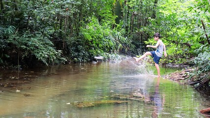 Um menino brincando nas &aacute;guas de um riacho na floresta