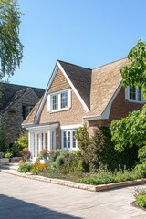 Beautiful brick house with a sloped roof and lush garden in a sunny suburban neighborhood during the clear afternoon of a summer day