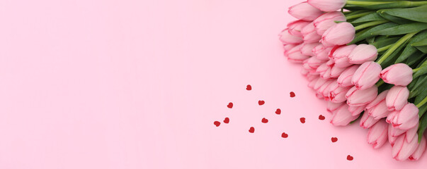Bouquet of beautiful tulip flowers and red paper hearts on pink background, top view. Banner design with space for text