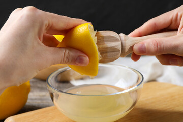 Woman juicing lemon into bowl at wooden table, closeup