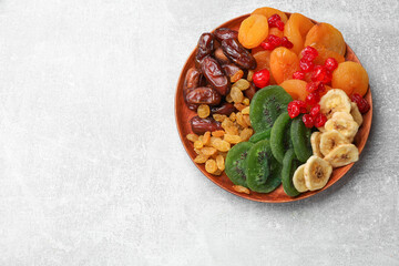Mix of different dried fruits in bowl on light grey table, top view. Space for text