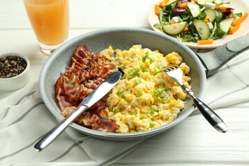Tasty brunch. Delicious scrambled eggs, bacon, salad and glass of juice served on white wooden table